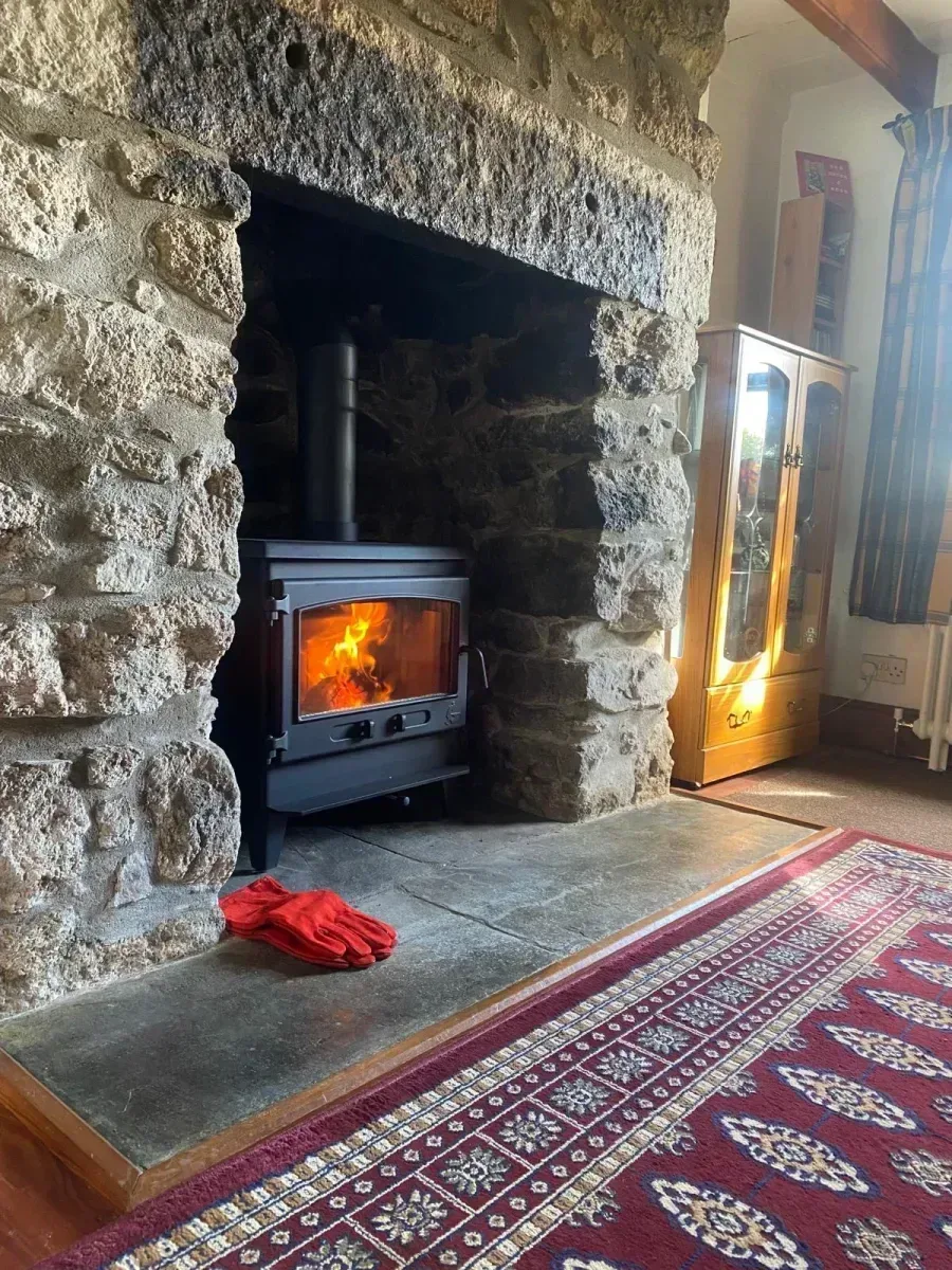 Black wood burning stove with roaring fire installed in rustic granite stone fireplace inglenook Cornwall
