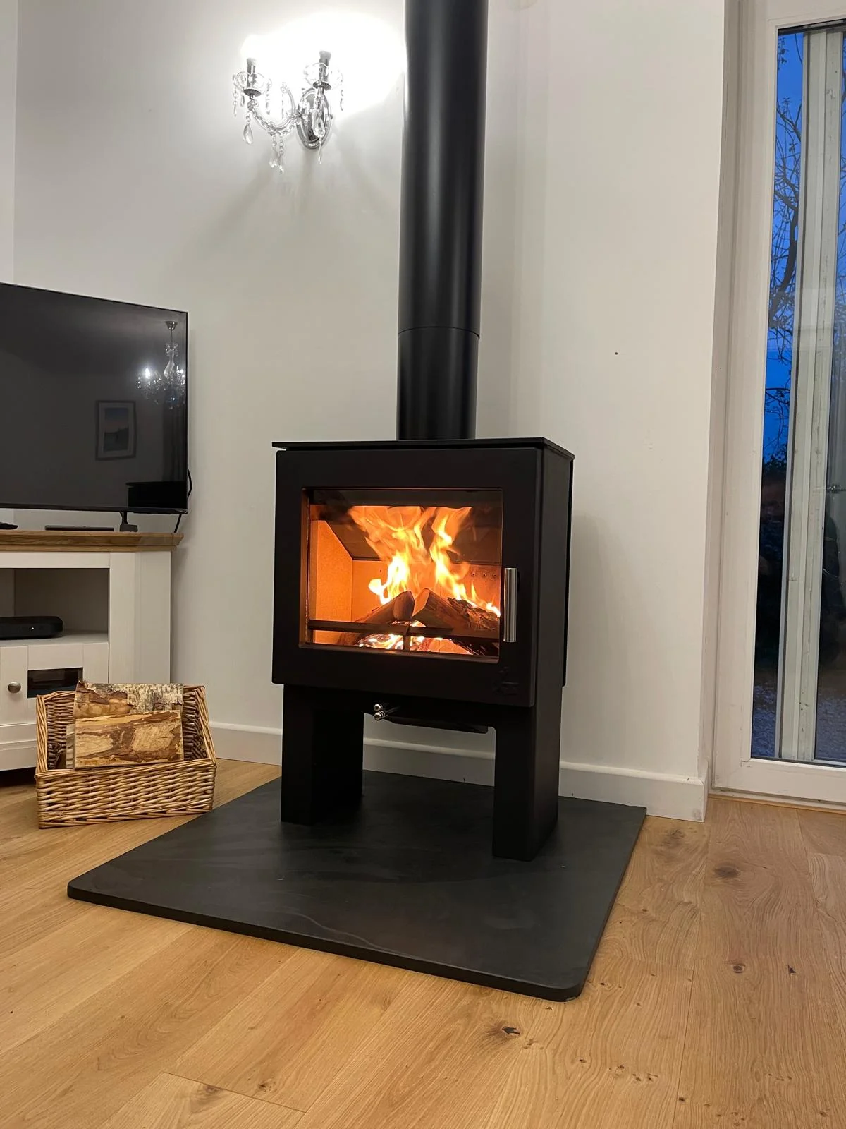 Modern black freestanding wood burning stove on steel hearth pad with roaring fire in contemporary living room
